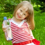 little girl standing in a grass holds in hand plastic bottle with mineral water